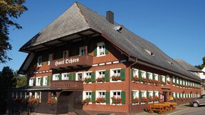 A traditional building with a sign reading "Hotel Ochsen." It features a steeply pitched roof, green shutters, and flower boxes on the windows. - Hotel Ochsen (Lenzkirch)