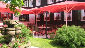 An outdoor seating area with red umbrellas, stone planters with flowers, and a building with windows and flower boxes. - Hotel Ochsen (Lenzkirch)