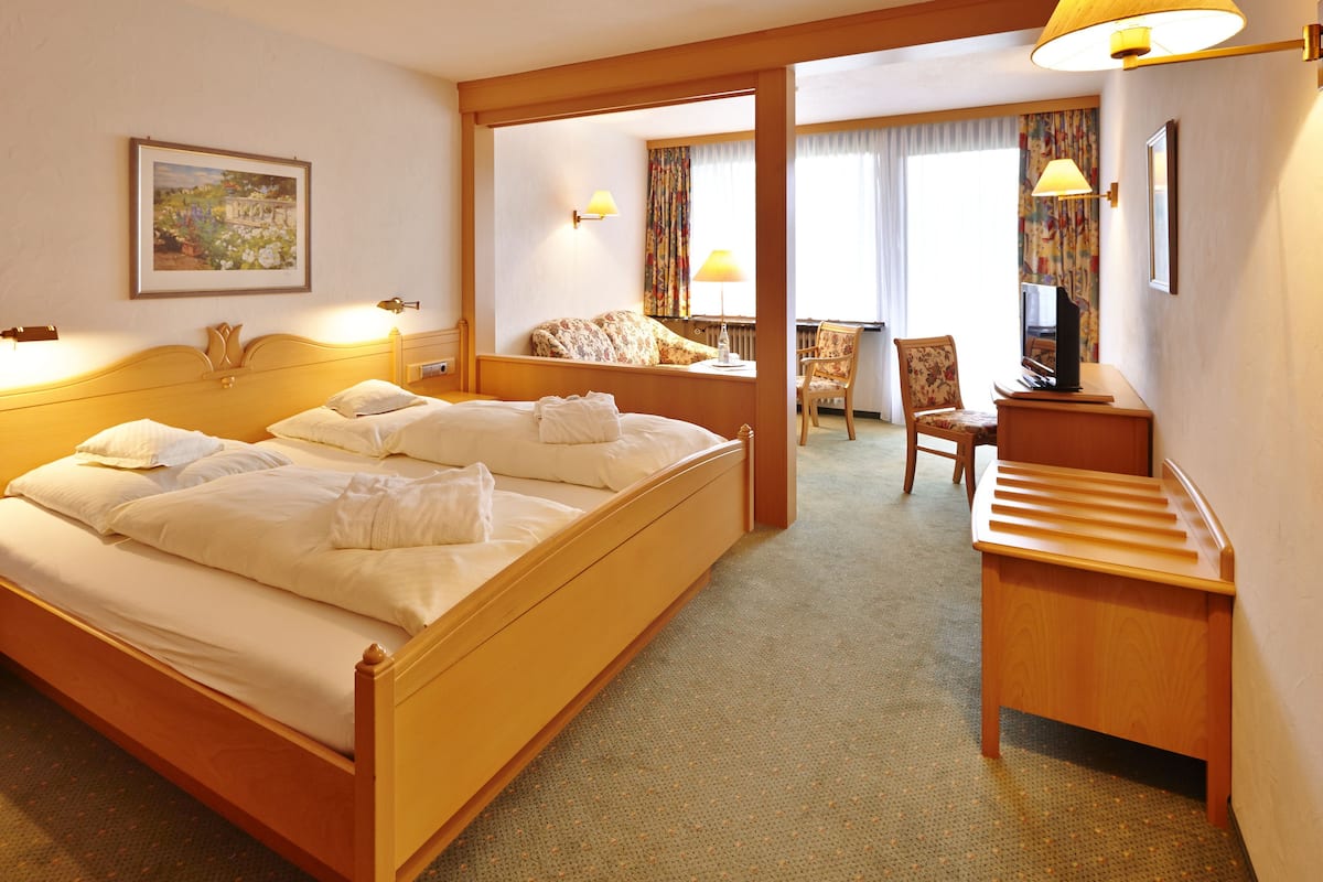 A hotel room with a large bed, bedside tables, a desk, a chair, and a painting on the wall.