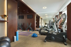 Un gimnasio con equipo de ejercicio, televisión y espejo.