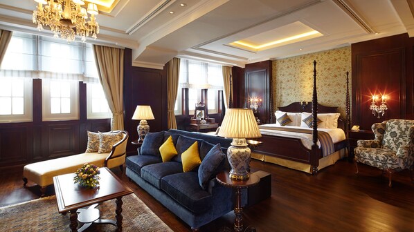 A spacious hotel room with a large bed, a sofa, a coffee table, and a chandelier.
