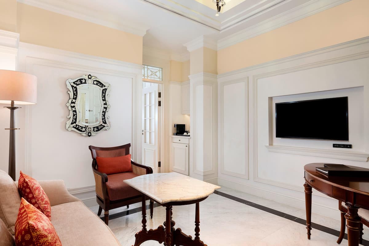 A living room with a sofa, a table, a chair, a TV, and a decorative mirror.