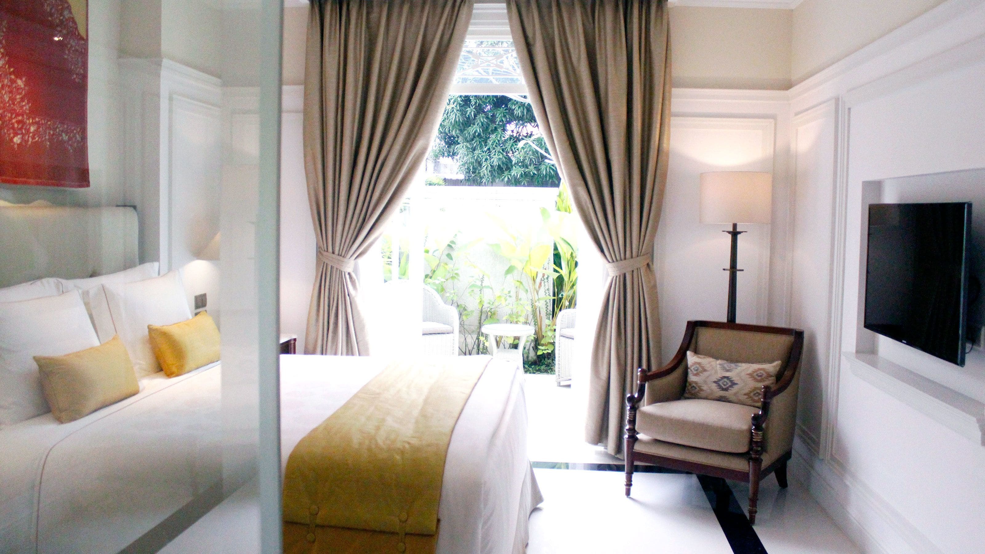 Habitación de hotel con cama, una silla, televisión y vista al exterior.
