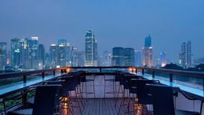 A rooftop terrace with a city skyline view, featuring a row of chairs and tables. - The Hermitage, A Tribute Portfolio Hotel, Jakarta (Jakarta)