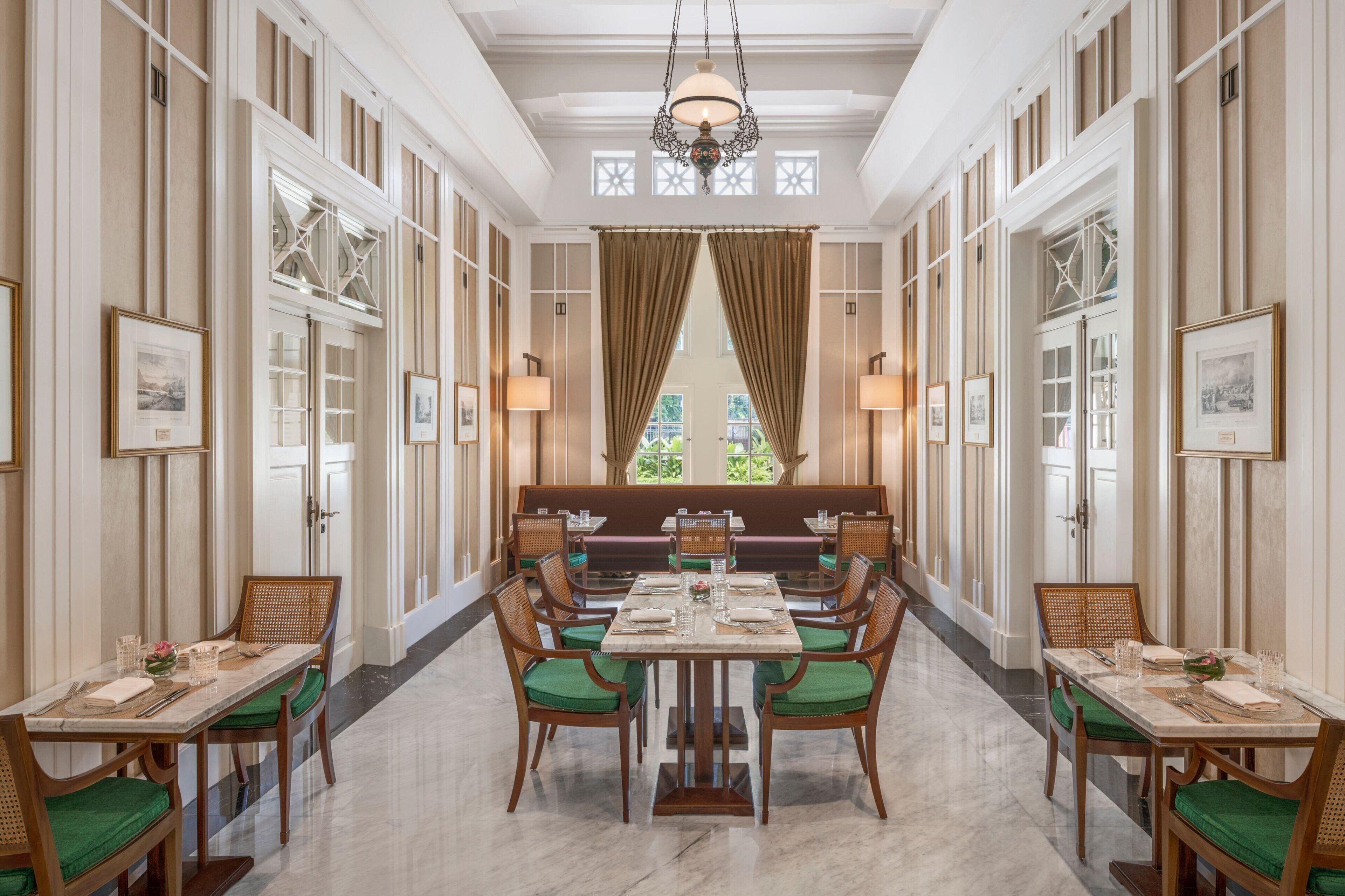 A formal dining area with a long table, green cushioned chairs, and framed artwork on the walls.