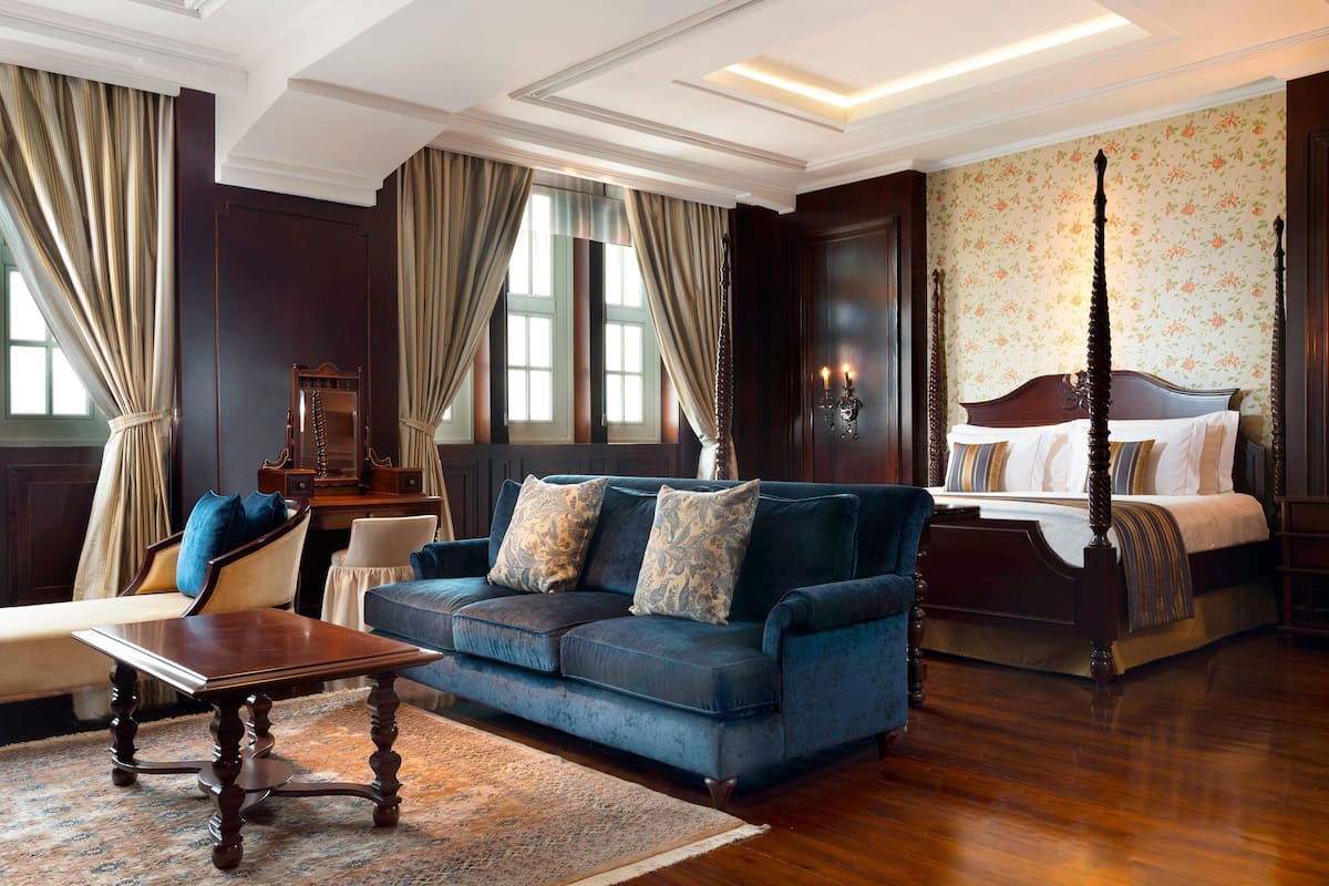 A room with a large bed, a sofa, a wooden coffee table, and a chair.