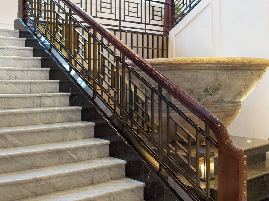 A marble staircase with a wooden handrail and black metal balusters.