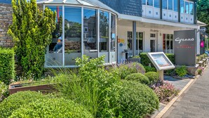 A hotel with a glass conservatory, a sign reading "Cyrano Hotel Restaurant," and a well-maintained garden with various plants and flowers. - RAVEL Hotel Cyrano (Waimes)