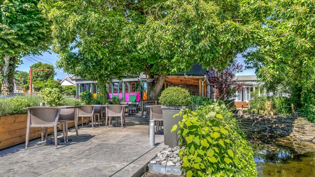 An outdoor patio with wicker furniture, a small pond, and a stone pathway. - RAVEL Hotel Cyrano (Waimes)