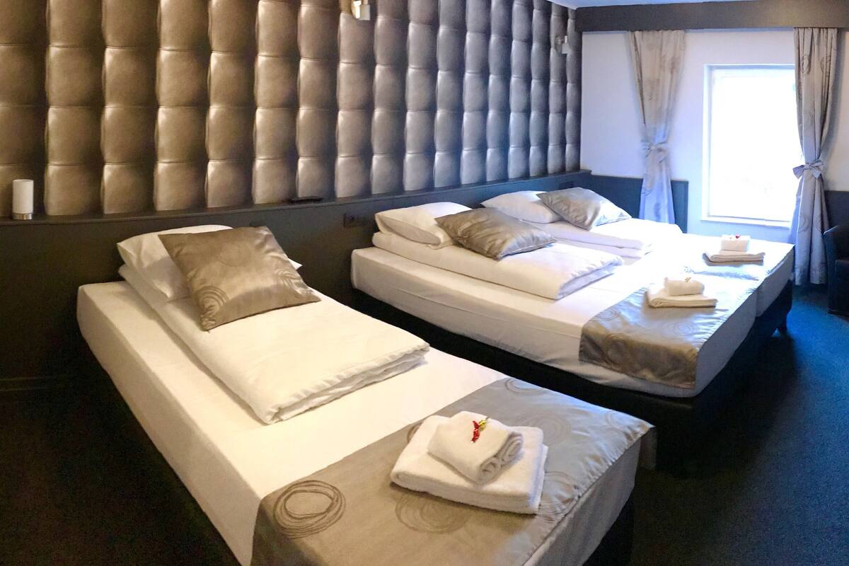 A hotel room with two single beds, a padded headboard, and a window with curtains.