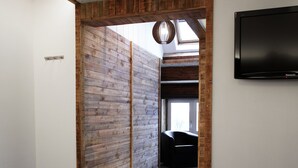 A modern hotel room with a wooden accent wall, a TV mounted on the wall, and a bed with white bedding. - RAVEL Hotel Cyrano (Waimes)