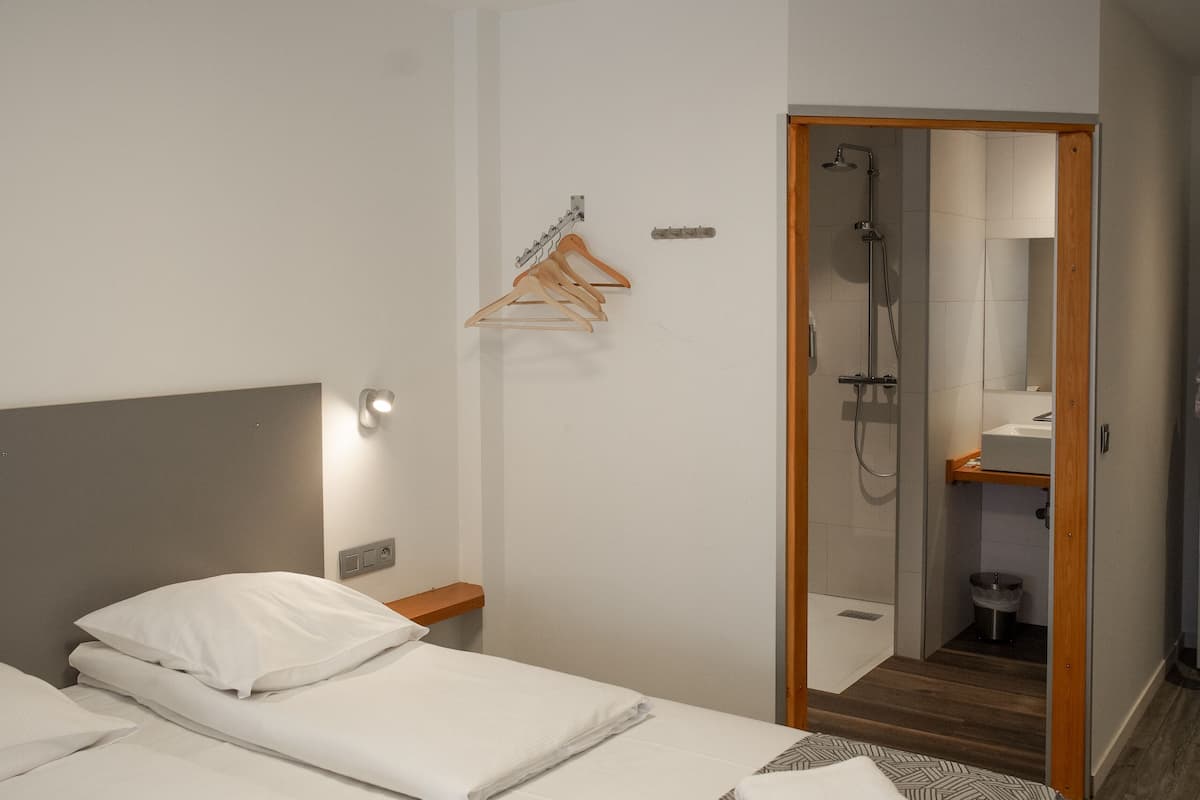 A hotel room with two beds, a shower, a wooden floor, and a hanging clothes rack.