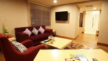 A living room with a red sofa, a coffee table, and a flat-screen TV mounted on the wall.