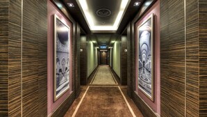 A hallway with a patterned carpet, framed artwork on the walls, and a ceiling with recessed lighting.