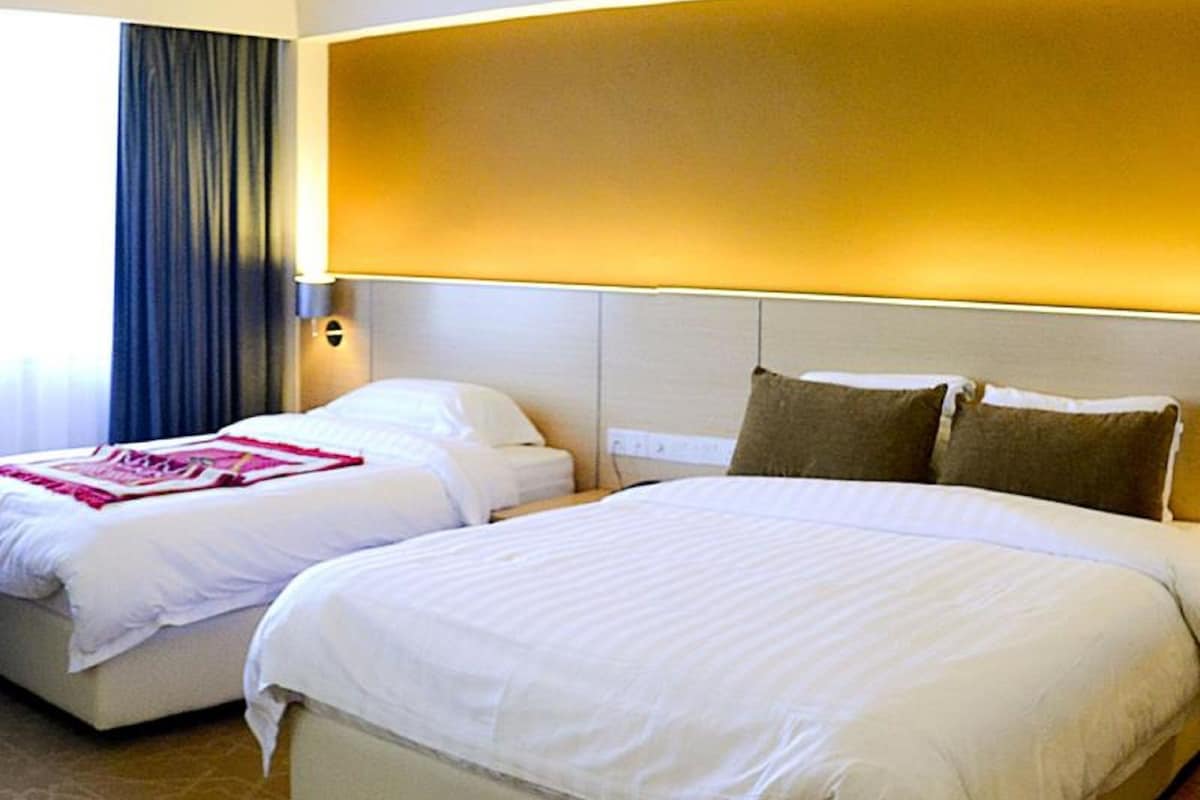 A hotel room with two beds, a large window with curtains, and a wall-mounted lamp.