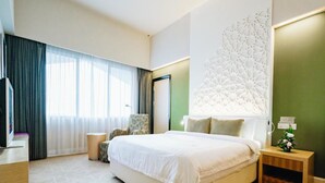 A modern hotel room with a large bed, a seating area with a chair, a small table, and a decorative wall panel.