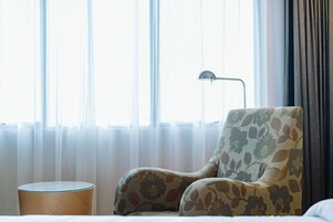 Une chambre d’hôtel avec un fauteuil à motifs floraux, une petite table d’appoint ronde en bois et une lampe sur pied.