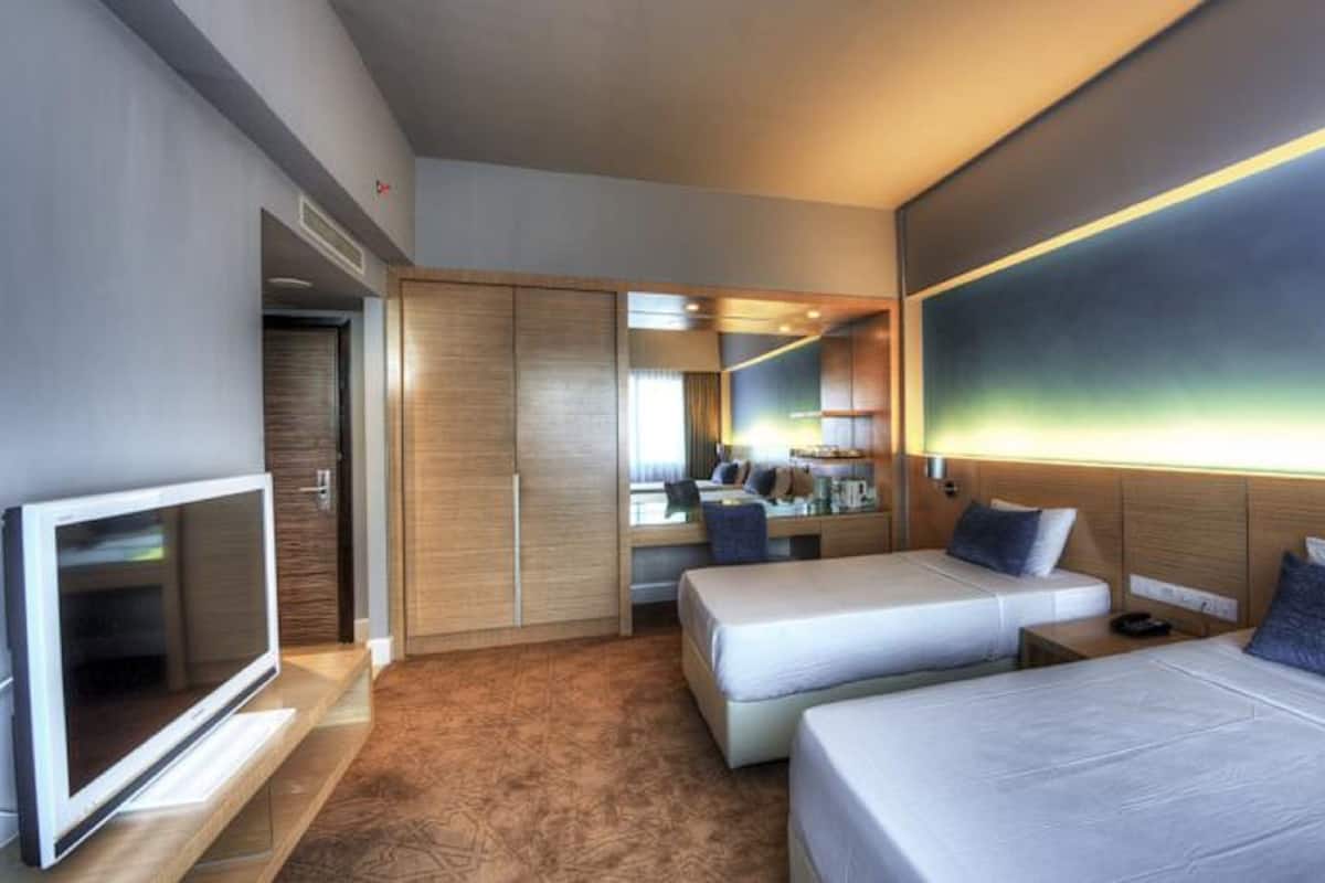 A hotel room with two beds, a TV, a wardrobe, and a mirror.