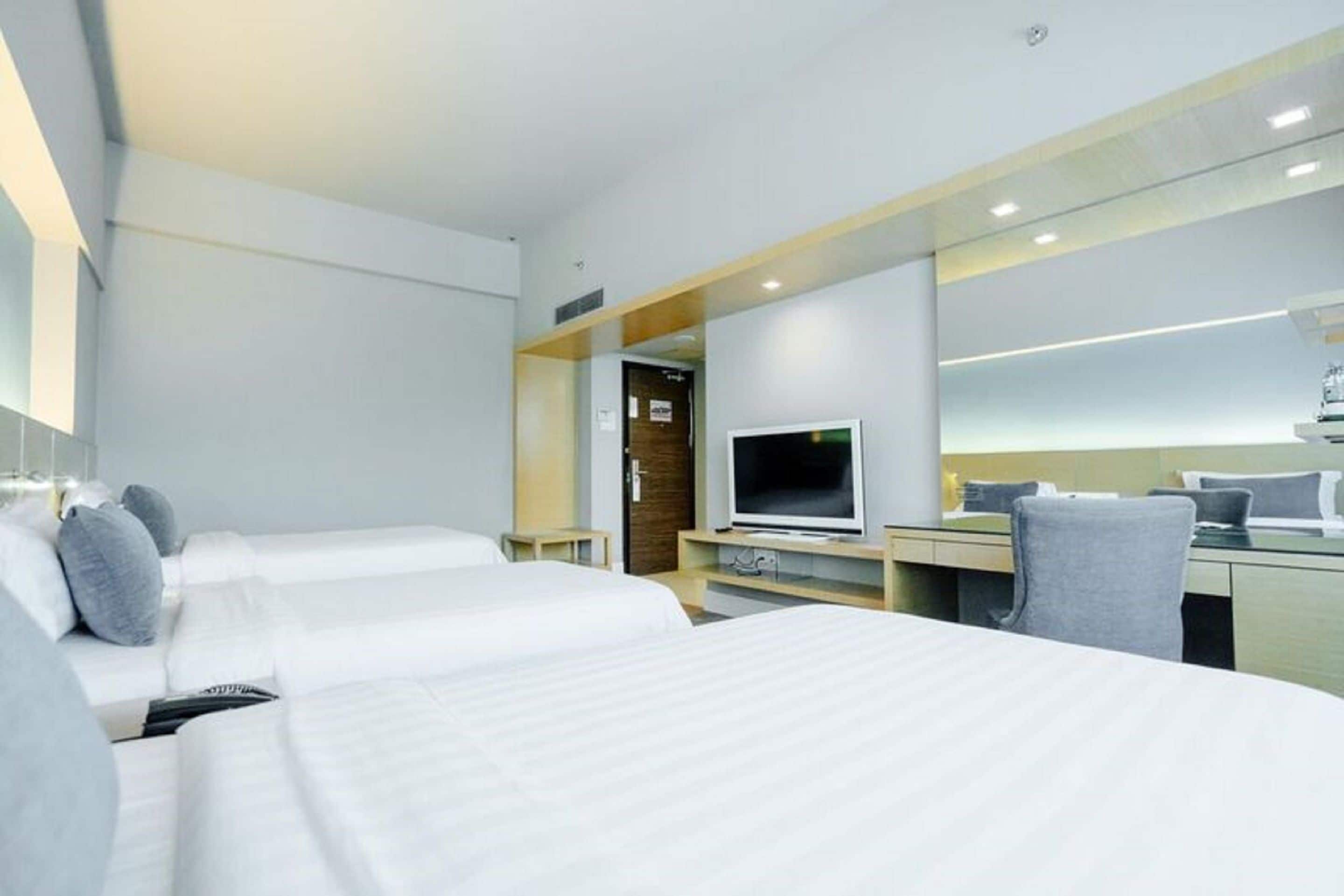 A modern hotel room with two beds, a TV, a desk, and a mirror.