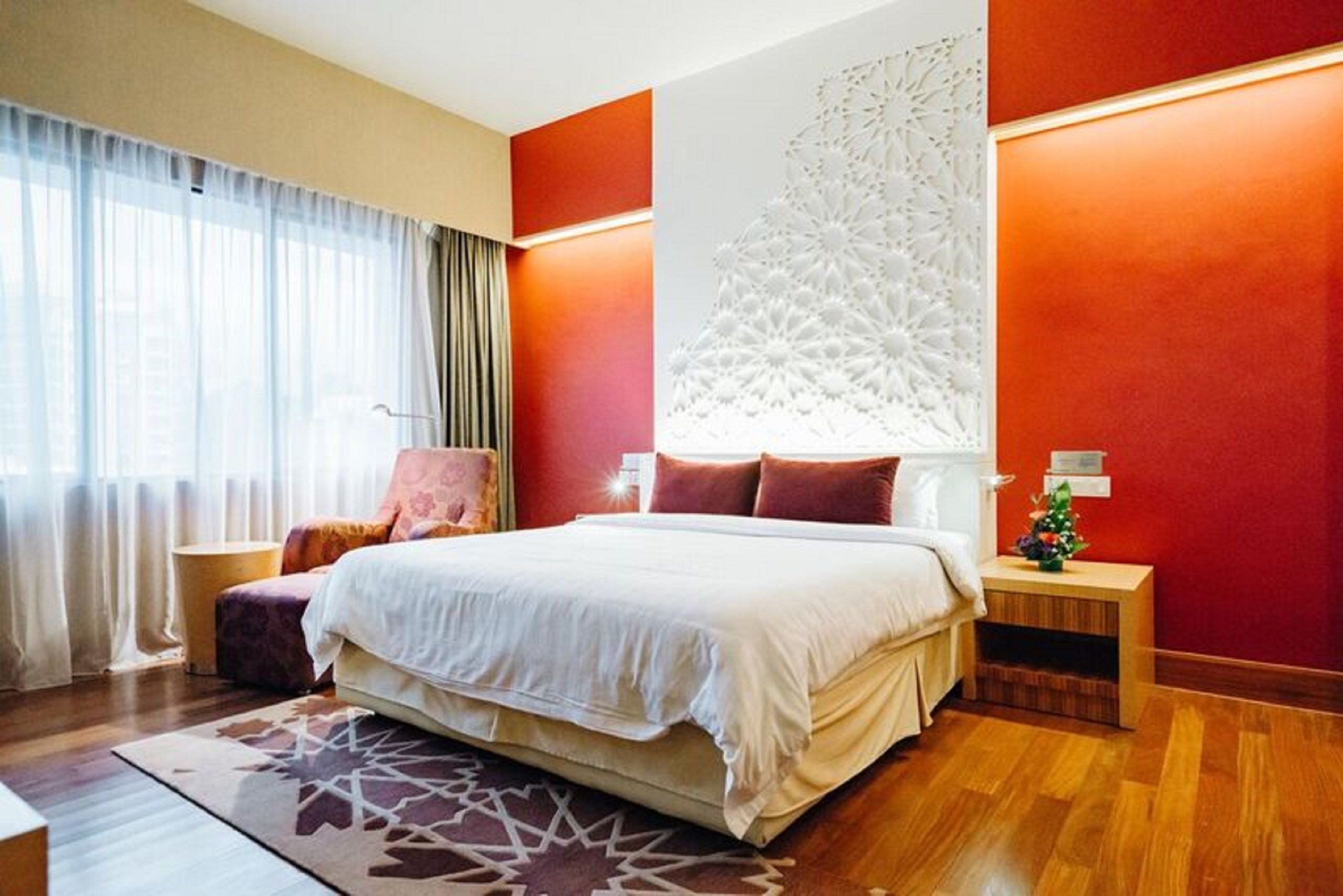 A modern hotel room with a large bed, a decorative wall panel, and a small side table with a plant.