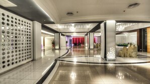 A modern hotel lobby with a polished floor, a reception desk, and a seating area with tables and chairs.