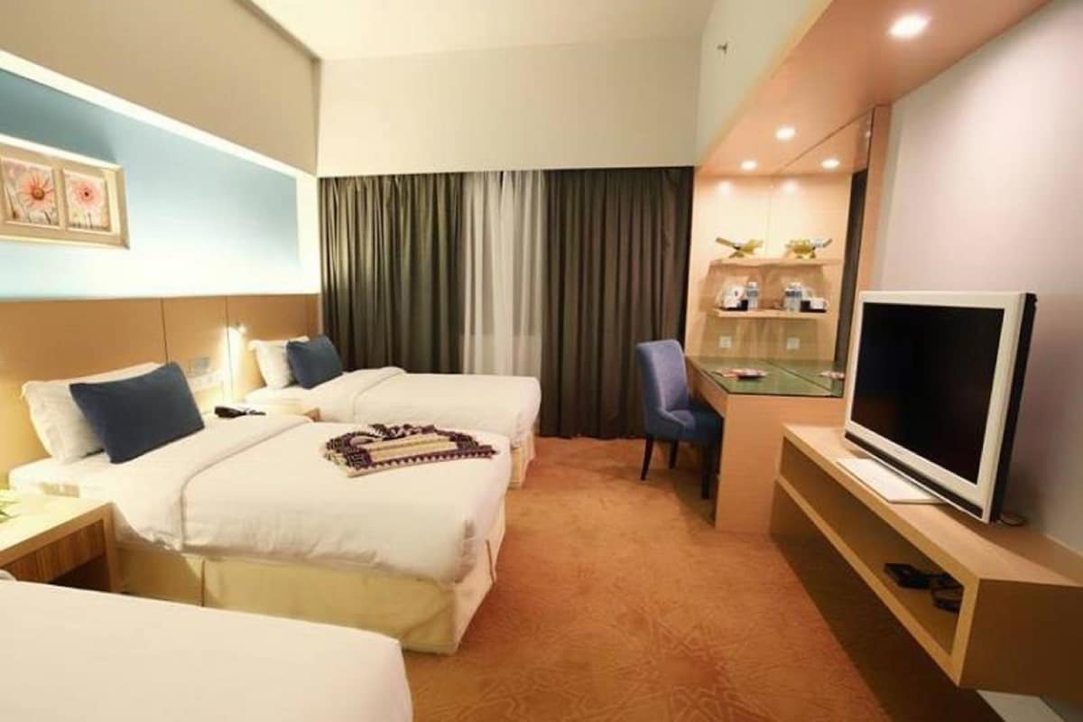 A hotel room with two beds, a desk, a chair, a TV, and a small shelf with toiletries.