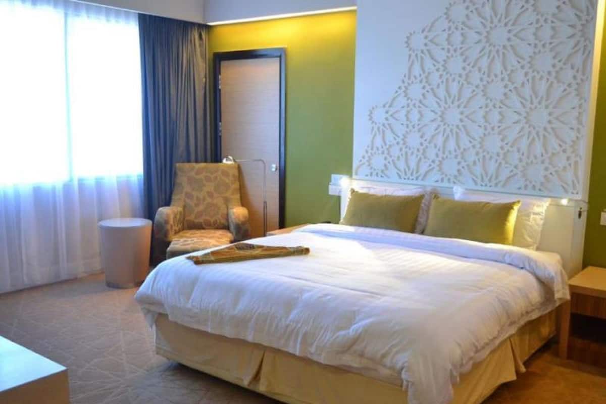 A hotel room with a large bed, a chair, a small table, and a decorative wall panel.