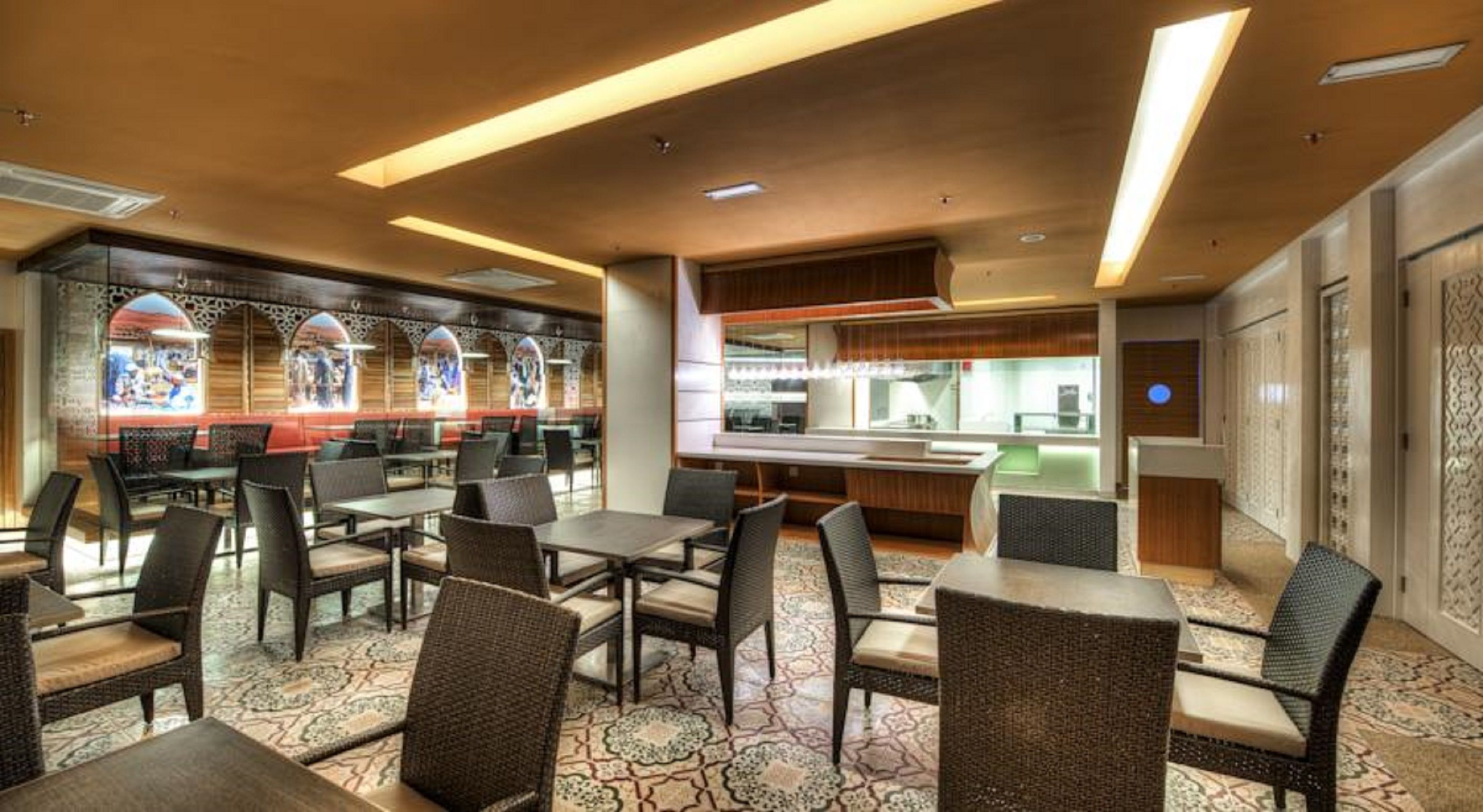 Un restaurante con una decoración moderna, que ofrece diferentes opciones de asientos como mesas y sillas, una cocina a la vista y detalles decorativos en las paredes.