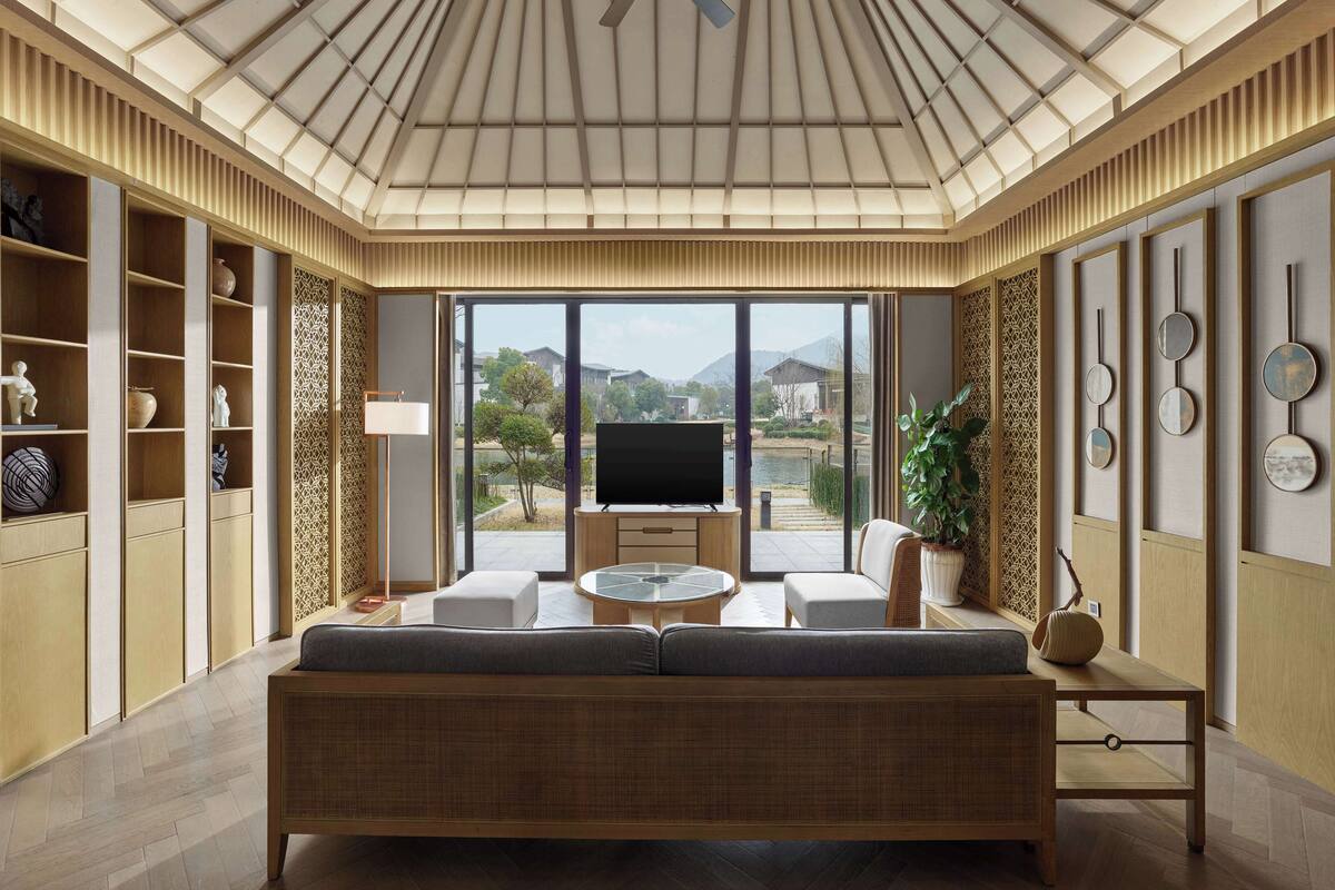 A modern living room with a large sofa, a TV, and a view of a lake and buildings.