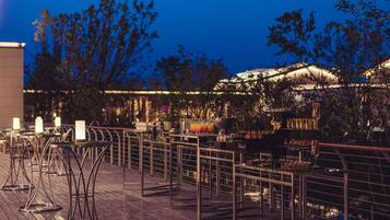 An outdoor dining area with tables and chairs, surrounded by a railing and trees.