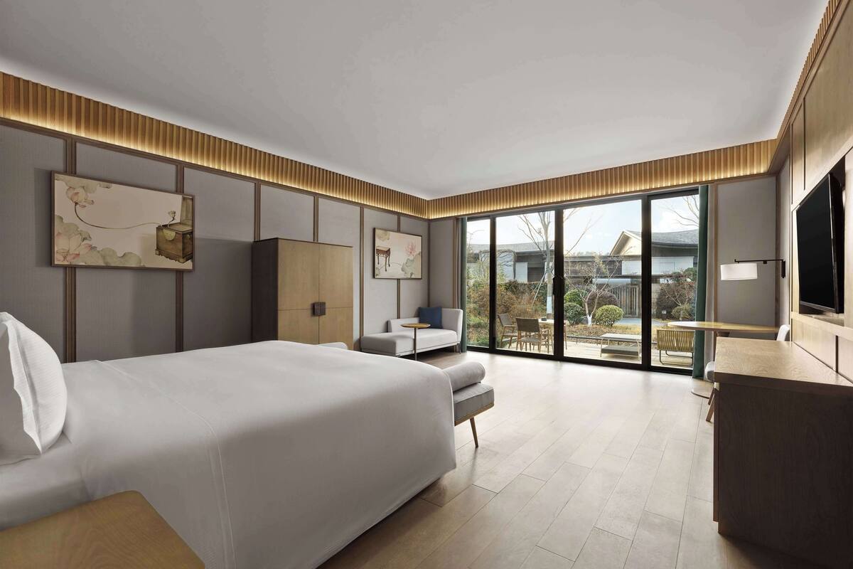 A modern hotel room with a large bed, a desk, and a view of the outdoors.