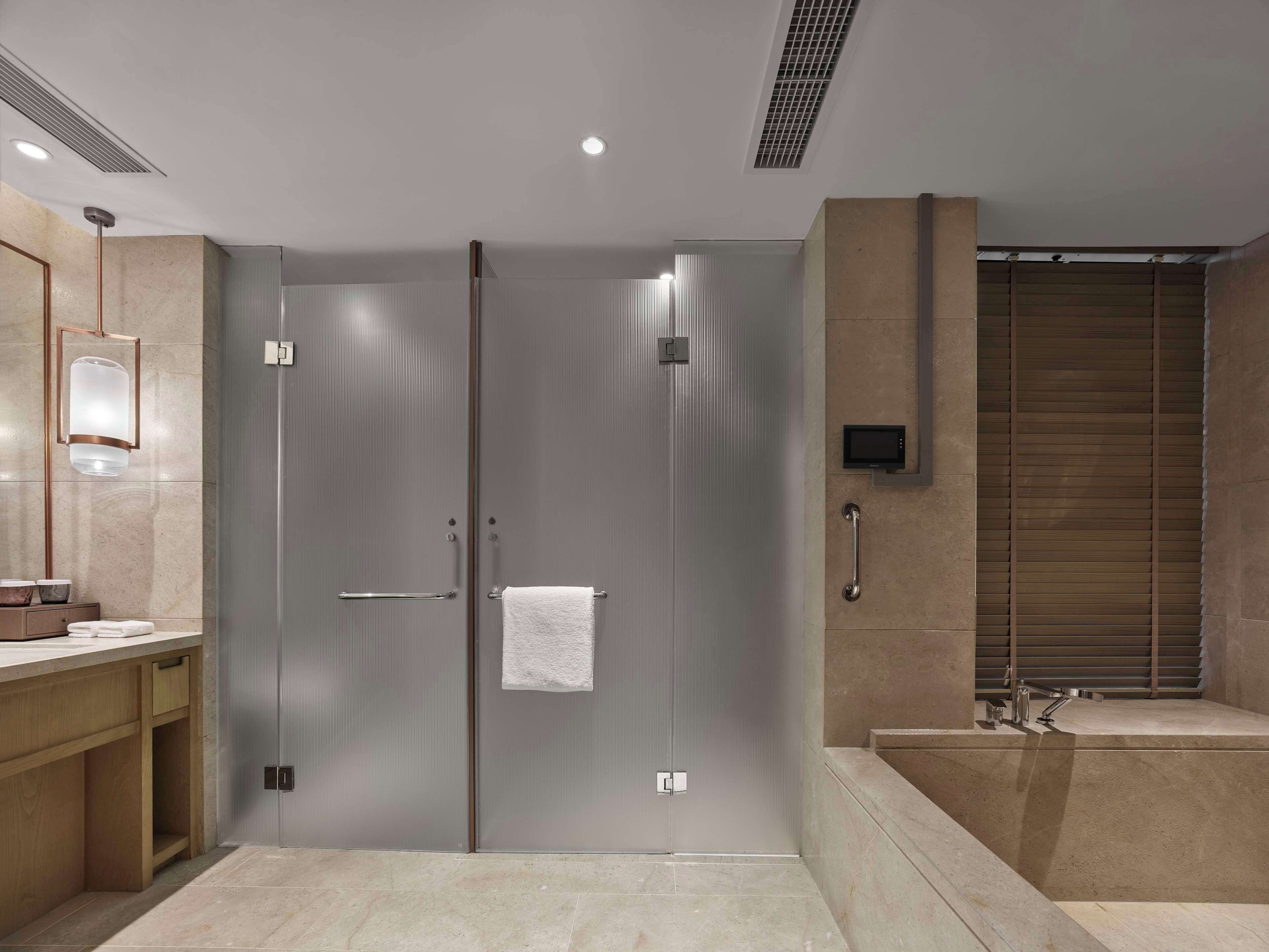 A modern bathroom with a double door, a towel hanging on the right door, a handheld showerhead, and a built-in sink.