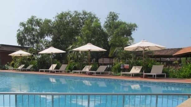 A swimming pool with lounge chairs and umbrellas. - The International Centre Goa (Panaji)