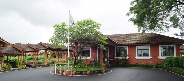A building with a red facade, multiple windows, and a flagpole with a flag. - The International Centre Goa (Panaji)