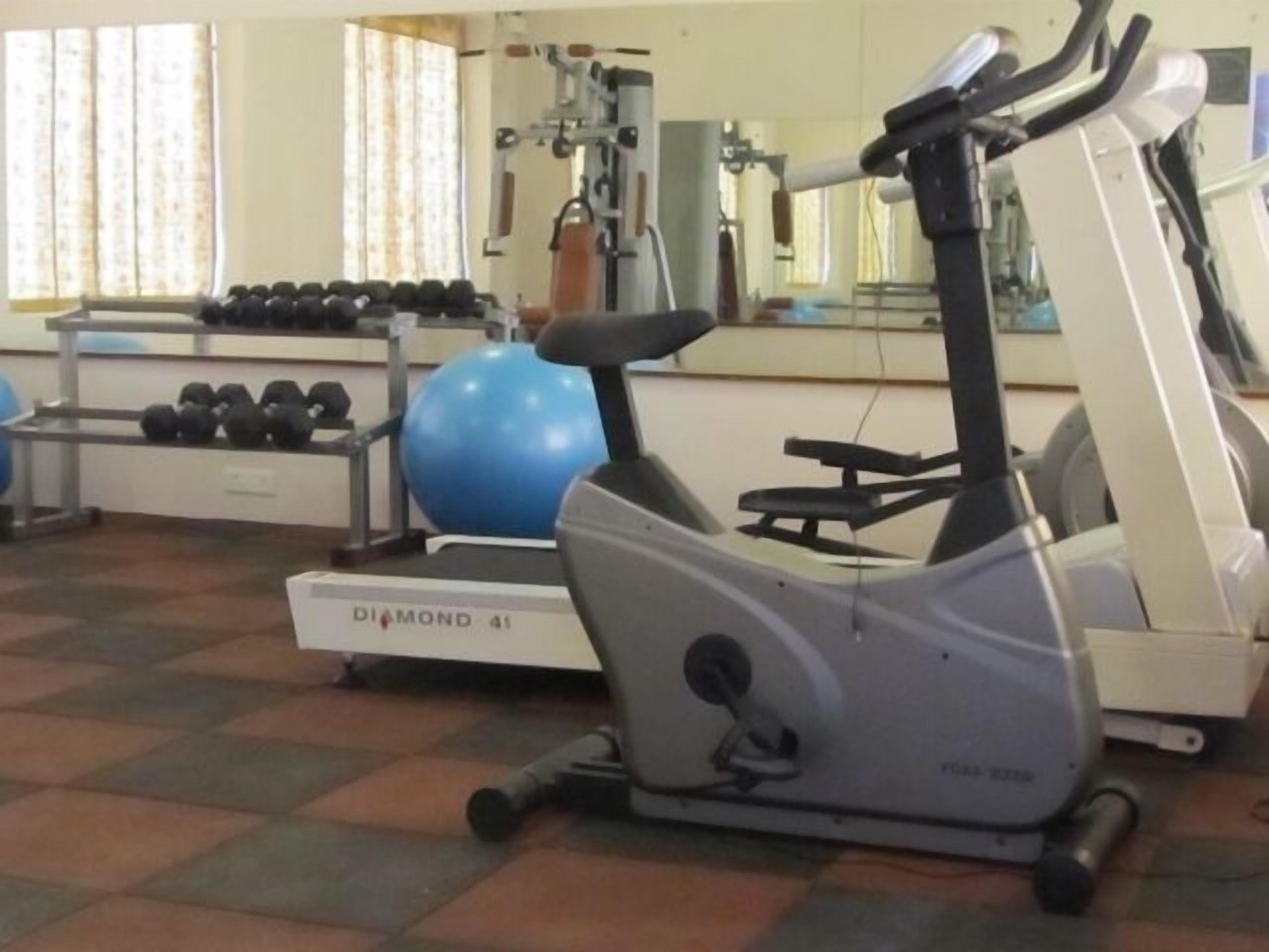 A gym with exercise equipment including a treadmill, dumbbells, and a blue exercise ball.