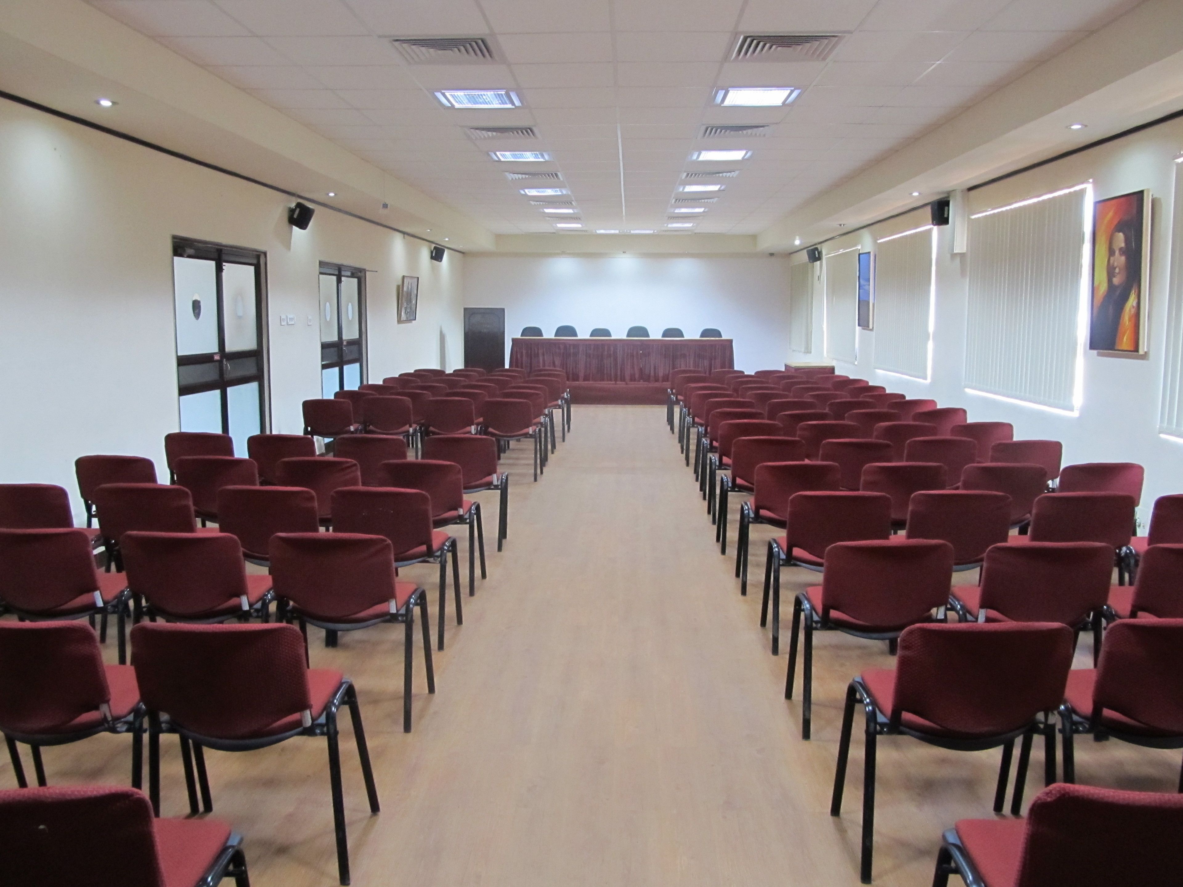 Una sala conferenze con file di sedie rosse rivolte verso un palco con una tovaglia rossa.