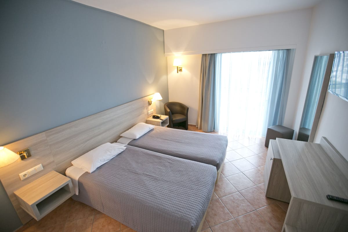 Ein Hotelzimmer mit zwei Betten, einem Schreibtisch, einem Stuhl, einem Nachttisch und einer Lampe.
