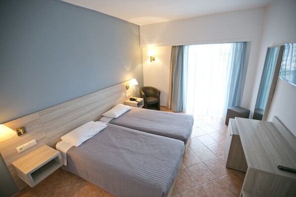 Una habitación de hotel con dos camas, un escritorio, una silla, una mesita de noche y una lámpara.