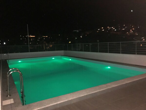 Una piscina rectangular con una escalera metálica en un lateral, rodeada por un muro bajo y una barandilla.