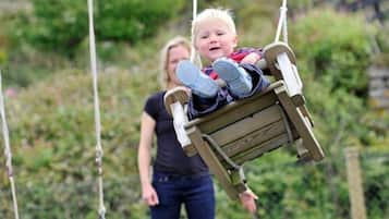 A child on a wooden swing with ropes, set against a backdrop of greenery.