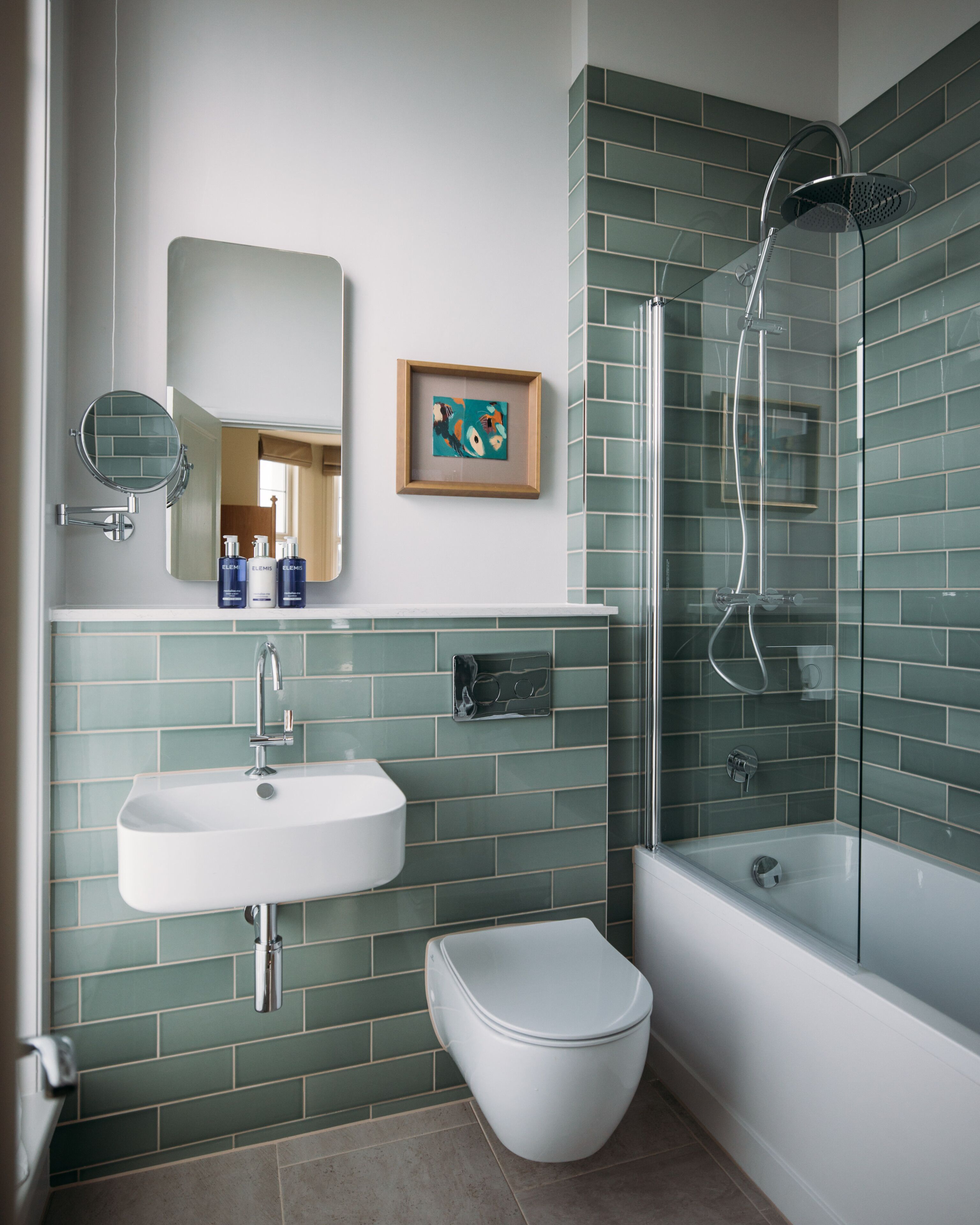 A modern bathroom with a sink, mirror, framed artwork, and a shower enclosure.