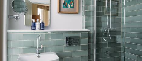 A modern bathroom with a sink, mirror, framed artwork, and a shower enclosure.