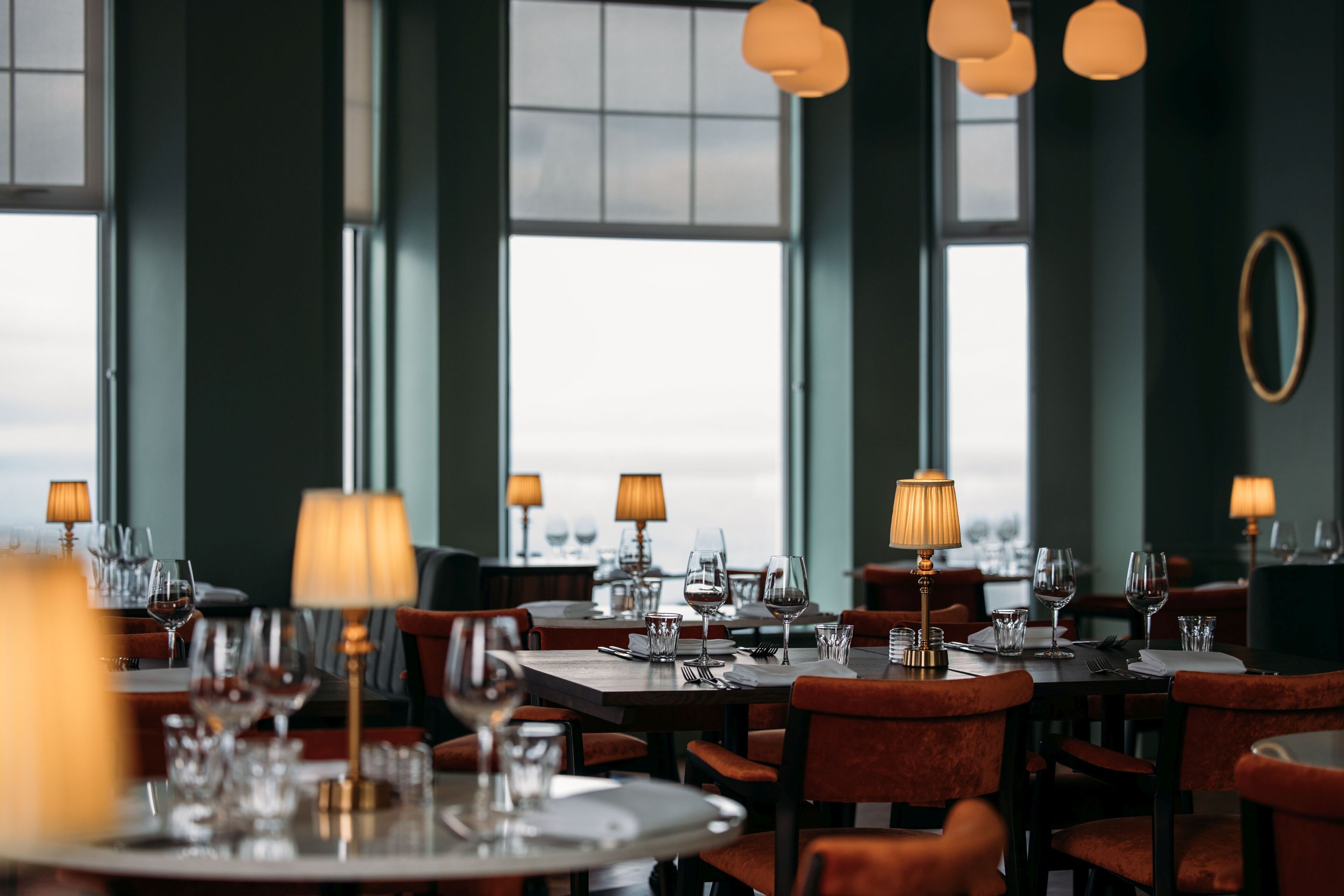 Un restaurante con mesas redondas, sillas y lámparas de mesa.
