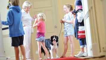 A group of people, including children and a dog, standing on a red carpet in a room with a door in the background.