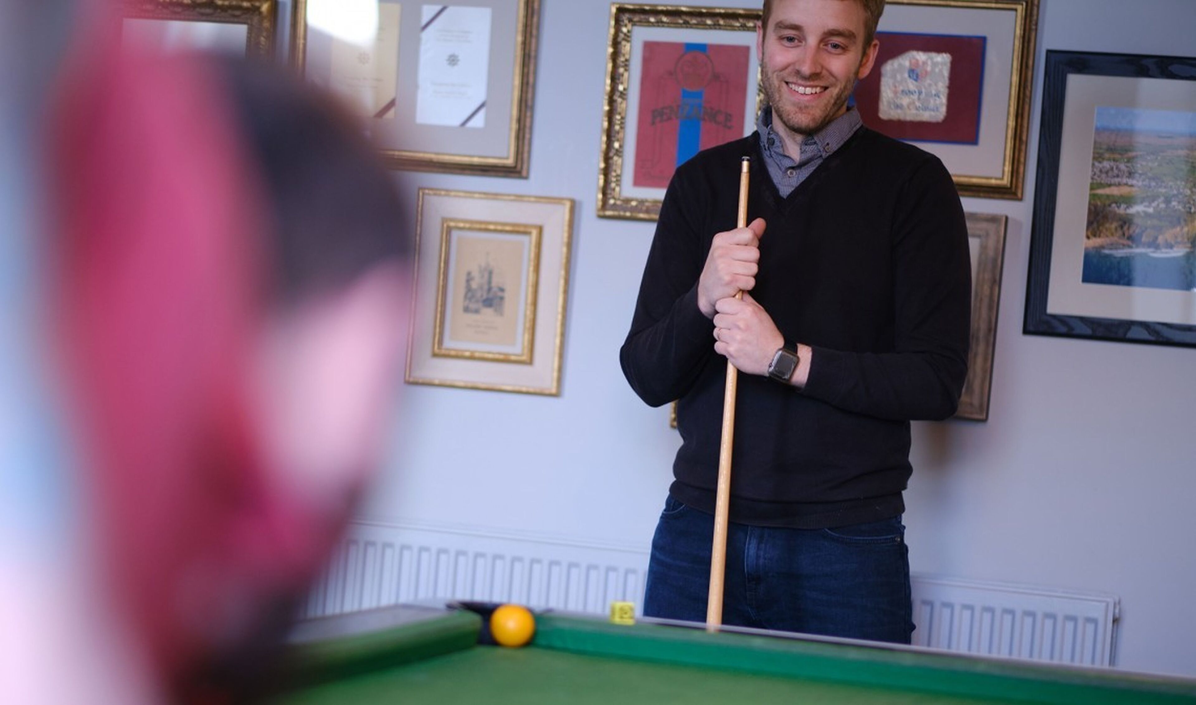 A person playing pool in a room with framed pictures on the wall.