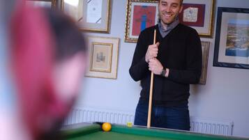 A person playing pool in a room with framed pictures on the wall.