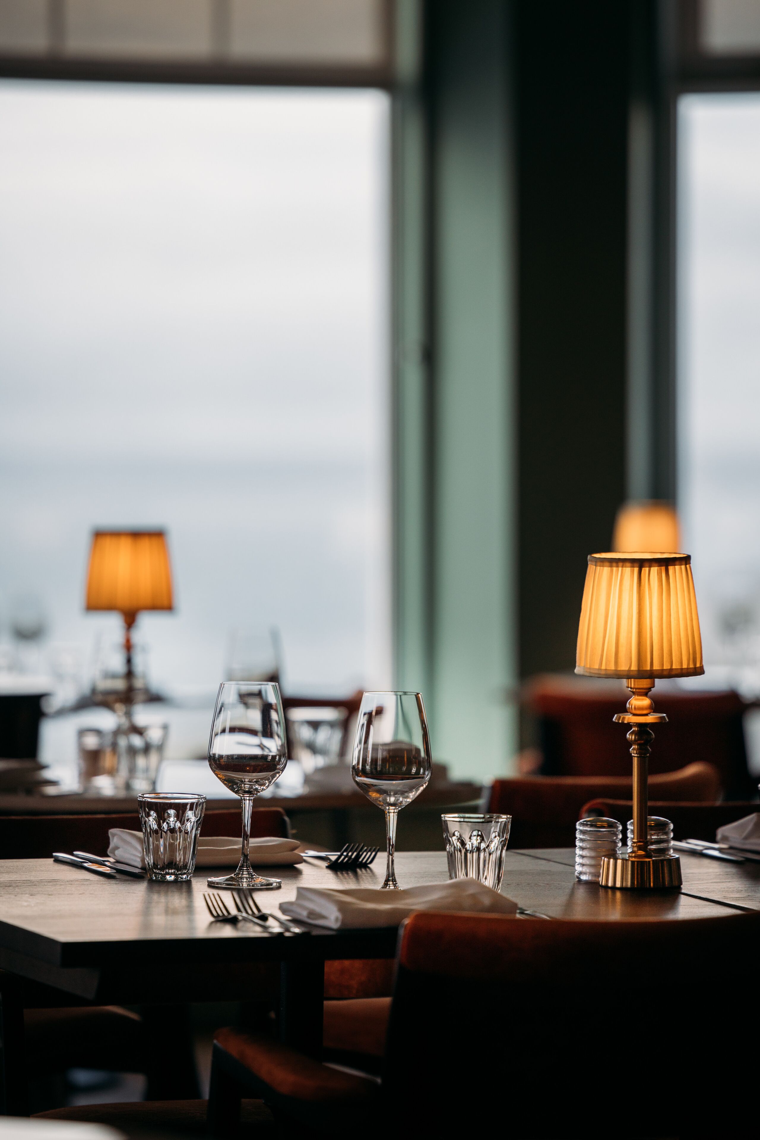 A restaurant table set with wine glasses, cutlery, and a lamp.
