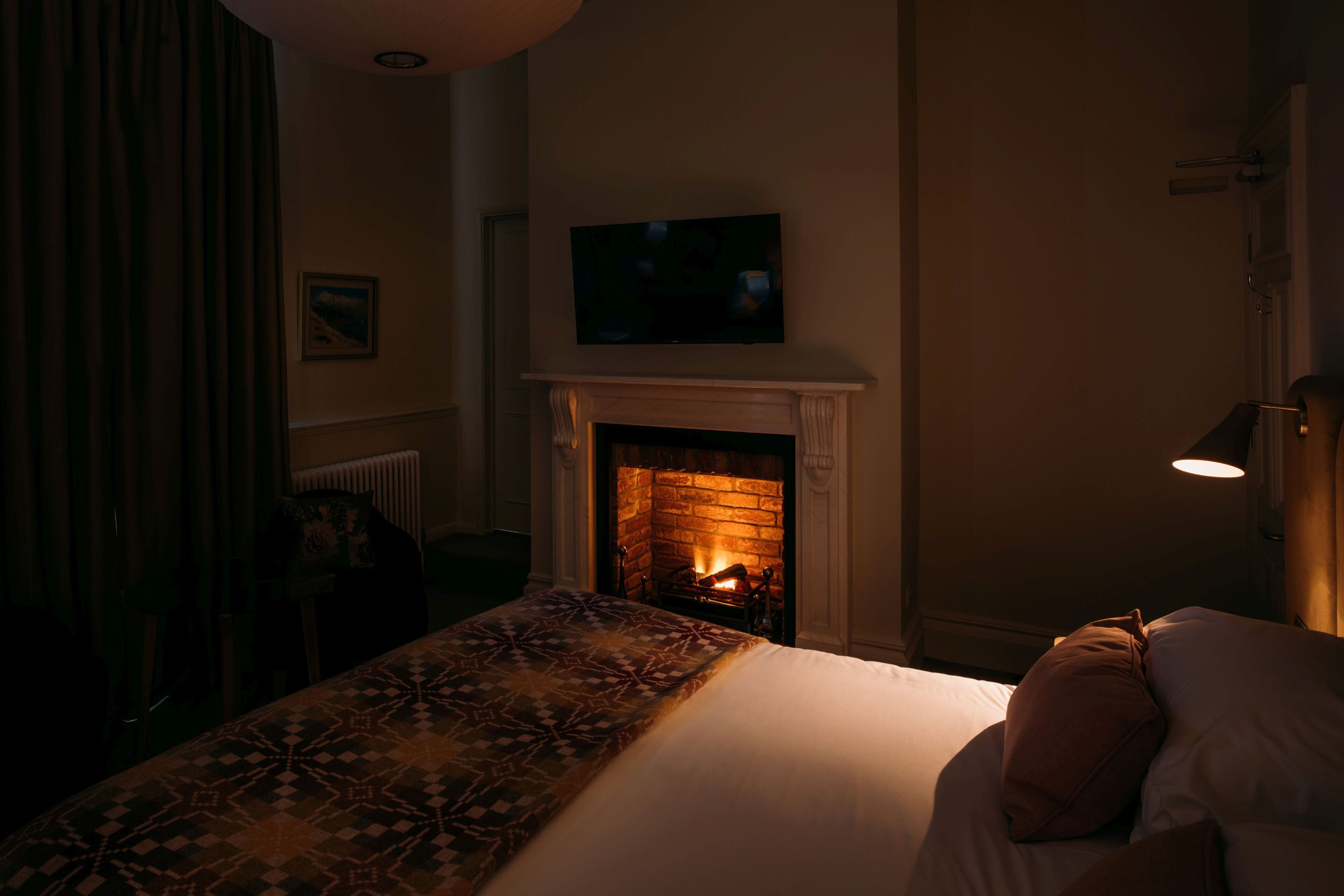 Ein Hotelzimmer mit Kamin, einem Bett mit gemustertem Überwurf und einem Bild an der Wand.