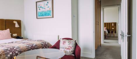 A hotel room with a bed, a chair, a table, and a painting on the wall.