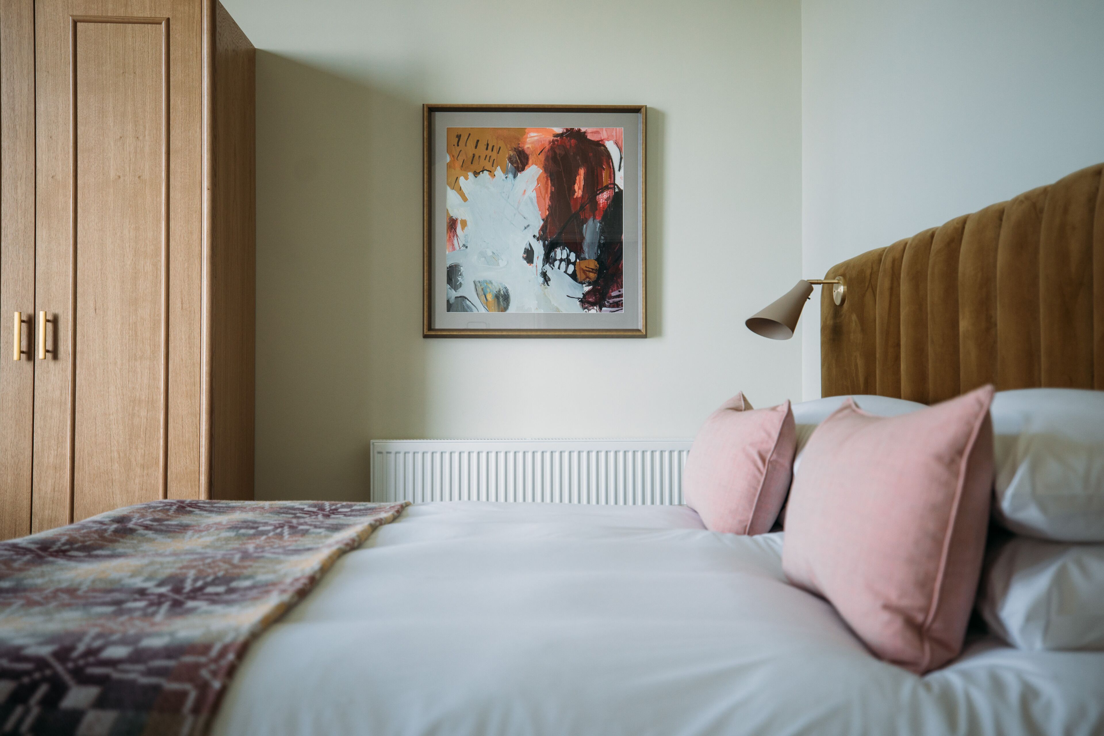 Une chambre à coucher comprenant un lit, un radiateur, une armoire en bois et un tableau abstrait encadré accroché au mur.